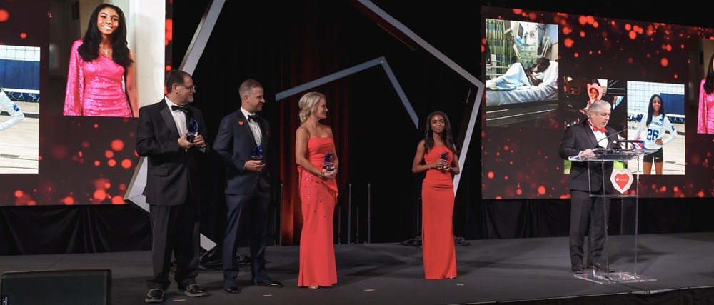 Jim Parisi, Scott and Carrie Greenberg, Alexa Roberts and TJ Tijerina in formal attire standing on stage holding awards.